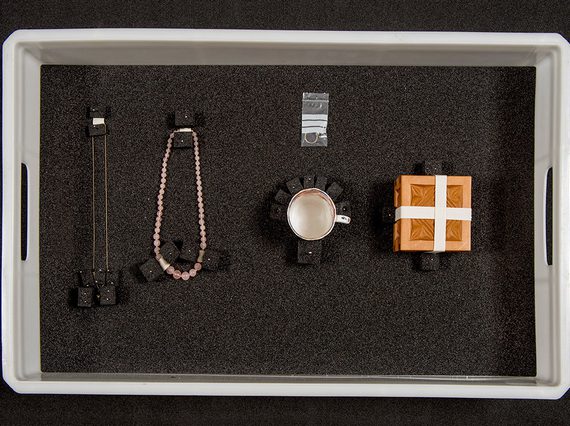 Two necklaces, a ring, a mug, and a wooden box packed in a plastic box with foam blocks.